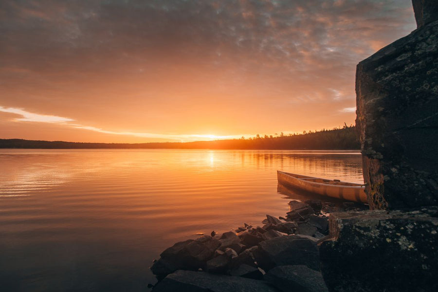 Yellow canoe moored beside a granite ledge on a calm lake at golden sunset
