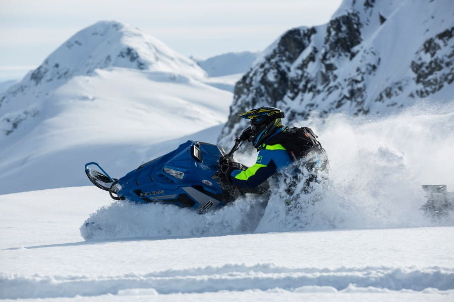 Rider carves a snowmobile through deep powder on a steep mountain slope